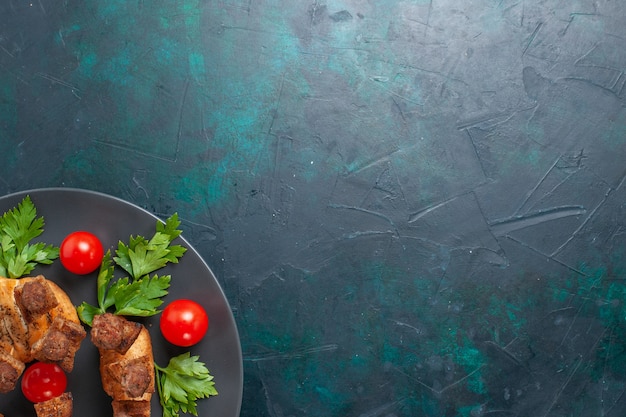 Vista dall'alto affettato di carne cotta con pomodorini verdi all'interno del piatto su sfondo blu scuro