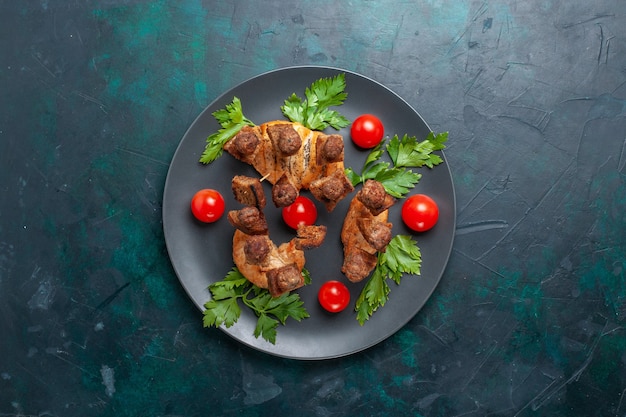 Vista dall'alto affettato di carne cotta con pomodorini verdi all'interno del piatto su sfondo blu scuro