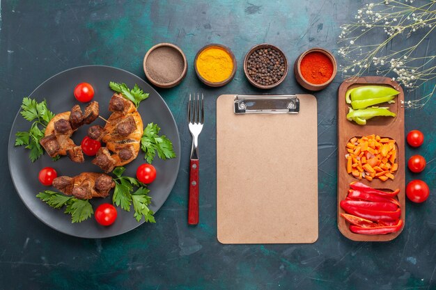 Vista dall'alto affettato di carne cotta con verdure e pomodorini all'interno della piastra con condimenti su sfondo blu scuro