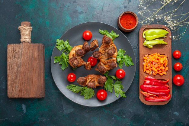 Vista dall'alto affettato di carne cotta con verdure e pomodorini all'interno della piastra su sfondo blu