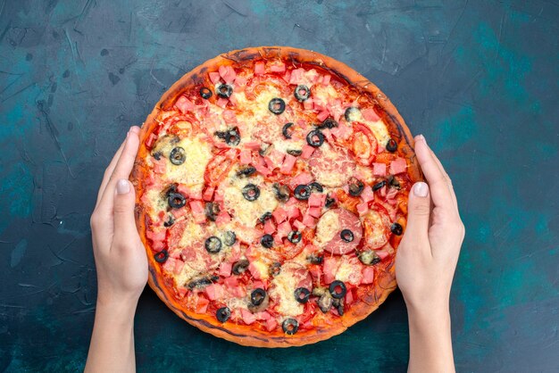 Vista dall'alto al forno deliziosa pizza con olive, salsicce e formaggio su sfondo blu.