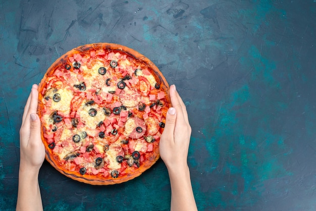 Vista dall'alto al forno deliziosa pizza con olive, salsicce e formaggio sulla scrivania blu.