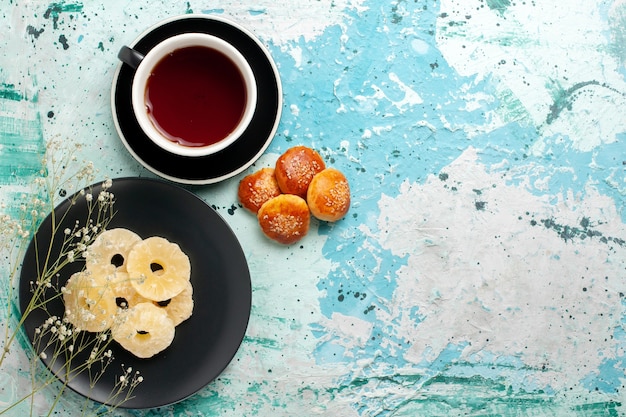 Vista dall'alto anelli di ananas essiccati all'interno del piatto con torte e tazza di tè su sfondo blu frutta ananas zucchero dolce secco