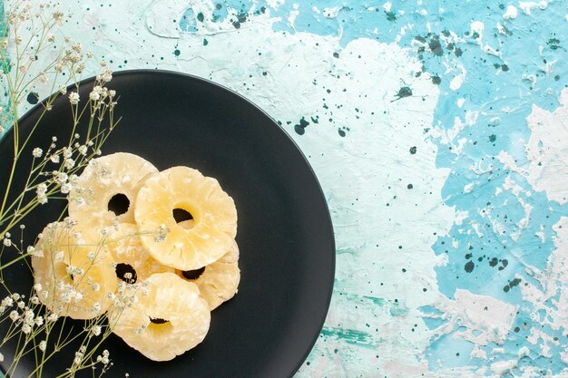 Vista dall'alto anelli di ananas essiccati all'interno della piastra su sfondo blu frutta ananas zucchero dolce secco