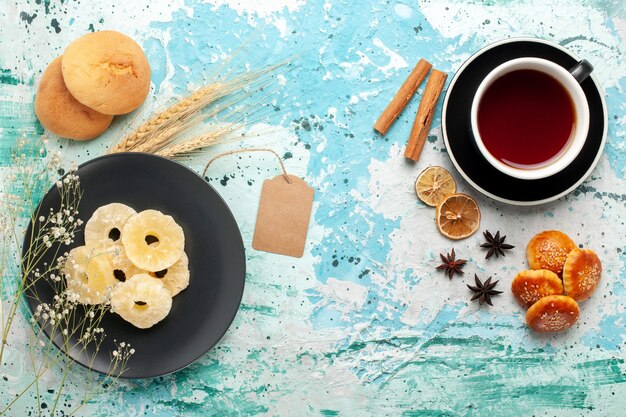 Vista dall'alto anelli di ananas essiccati con piccoli biscotti e tazza di tè su sfondo blu torta cuocere biscotti alla frutta biscotti di zucchero dolce