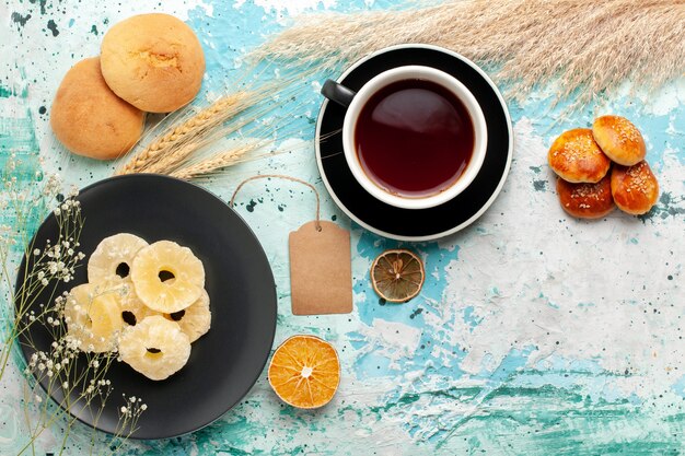 Vista dall'alto anelli di ananas essiccati con una tazza di tè sulla torta blu scrivania cuocere biscotti alla frutta biscotti di zucchero dolce