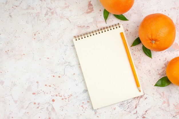 Vista dall'alto arance fresche arancia matita sul blocco note sulla luminosa superficie isolata con spazio libero