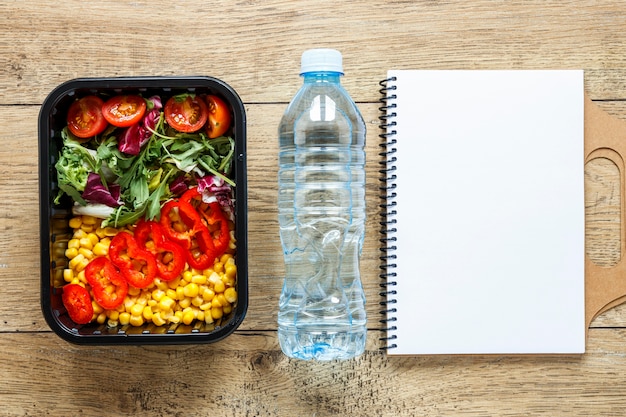 Vista dall'alto assortimento di alimenti in lotti cucinati con taccuino vuoto e acqua