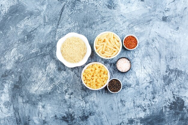 Vista dall'alto assortiti di pasta in ciotole con spezie su intonaco grigio Sfondo. orizzontale