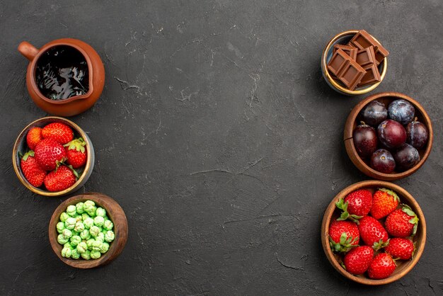 Vista dall'alto bacche e dolci salsa al cioccolato fragole cioccolato caramelle verdi e frutti di bosco in ciotole marroni sul tavolo