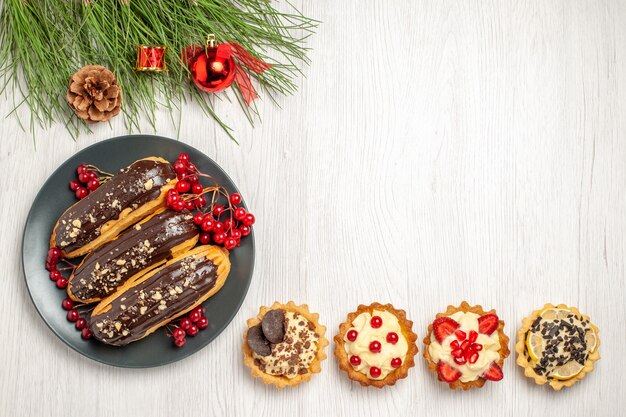 Vista dall'alto bignè al cioccolato e ribes sulle torte della piastra grigia sul fondo e foglie di pino con giocattoli di Natale sul terreno in legno bianco