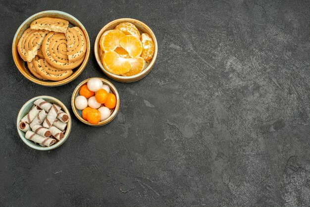 Vista dall'alto biscotti dolci con caramelle e mandarini sulla scrivania grigia