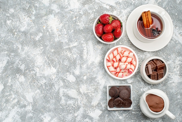 Vista dall'alto biscotti fragole cacao e cioccolatini e tè con cannella sul lato destro del tavolo grigio-bianco