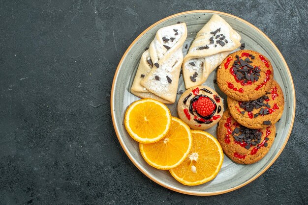 Vista dall'alto biscotti gustosi con pasticcini fruttati e fette d'arancia sullo sfondo scuro torta di frutta dolce torta di tè zucchero