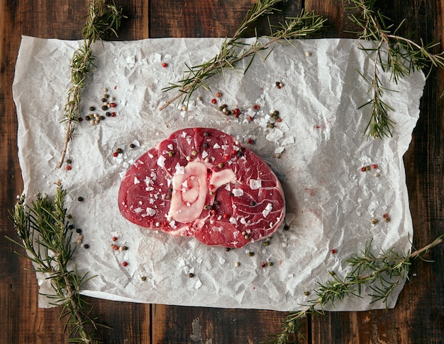 Vista dall'alto bistecca di carne con osso su carta artigianale, salata. pepato e con romero