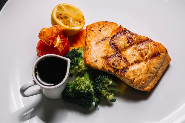 Vista dall'alto bistecca di pesce rosso alla griglia con broccoli una fetta di pomodoro al limone e salsa narsharab