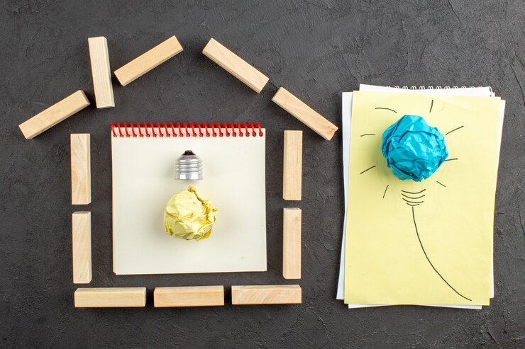 Foto gratuito vista dall'alto blocchi di legno a forma di casa obiettivi scritti su idea blocco note lampadina su carta su nero