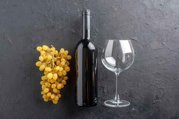 Vista dall'alto bottiglia di vino con uva gialla e apribottiglie in vetro sul tavolo scuro