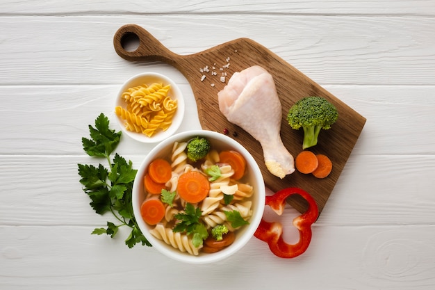 Vista dall'alto broccoli carote e fusilli in una ciotola con coscia di pollo sul tagliere