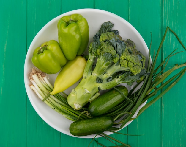 Vista dall'alto broccoli con cetrioli cipolle verdi e peperoni in un piatto su uno sfondo verde