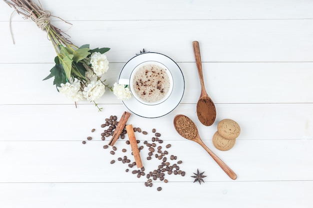 Vista dall'alto caffè in tazza con caffè macinato, spezie, chicchi di caffè, biscotti, fiori su fondo in legno. orizzontale