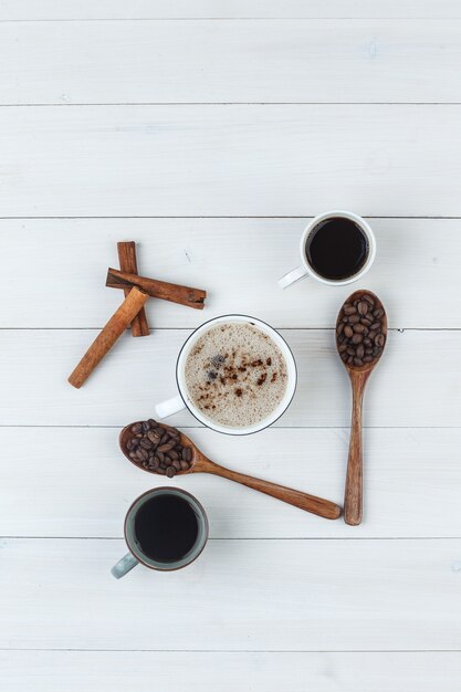 Vista dall'alto caffè in tazze con chicchi di caffè, bastoncini di cannella su fondo in legno. verticale