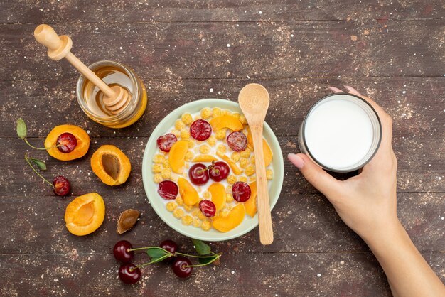 Vista dall'alto cereali con latte all'interno della piastra con frutta fresca miele e bicchiere di latte su legno, cereali cereali colazione