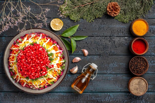 Vista dall'alto cibo gustoso cinque ciotole di spezie colorate Piatto di Natale aglio bottiglia di olio limone accanto ai rami di abete rosso con coni