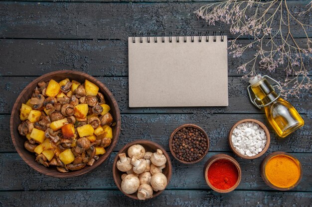 Vista dall'alto cibo sul piatto da tavola di patate e funghi accanto a una ciotola di funghi bianchi notebook spezie diverse e olio in bottiglia