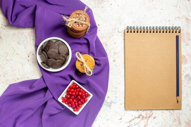 Vista dall'alto cioccolato e frutti di bosco in ciotole biscotti a scialle viola legati con corda matita e taccuino