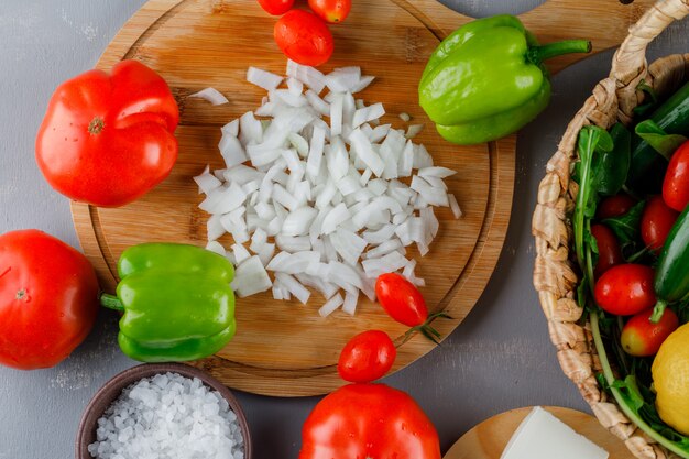 Vista dall'alto cipolle tritate sul tagliere con pomodori, sale, pepe verde sulla superficie grigia