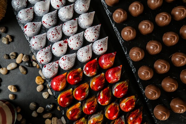 Vista dall'alto colorati cioccolatini decorativi su un supporto con pietre su uno sfondo nero