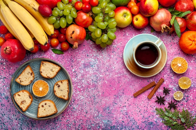 Vista dall'alto composizione di frutta fresca frutta colorata con deliziose torte a fette e tè sulla scrivania rosa