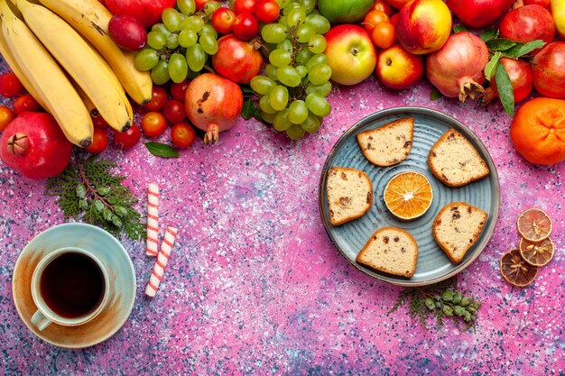 Vista dall'alto composizione di frutta fresca frutta colorata con torte a fette e tazza di tè sulla superficie rosa