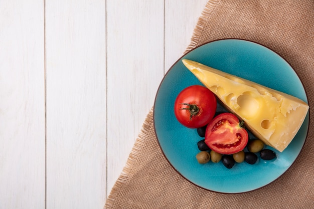 Vista dall'alto copia spazio formaggio maasdam con pomodori e olive su un piatto blu su un tovagliolo beige su sfondo bianco