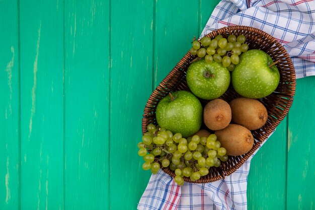 Vista dall'alto copia spazio mele verdi con kiwi e uva in cesti su un asciugamano a scacchi su uno sfondo verde