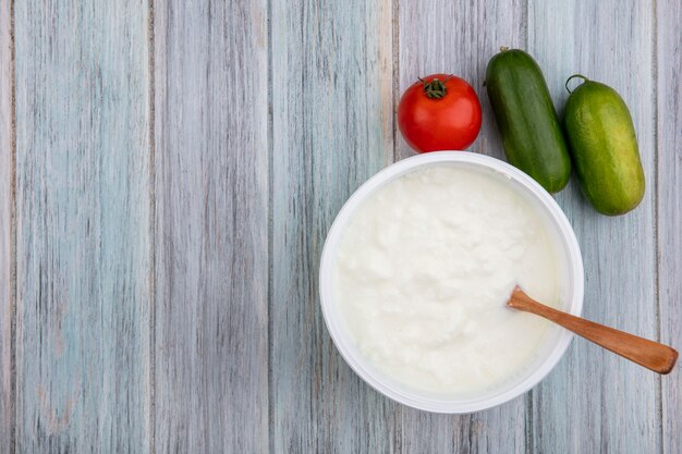 Vista dall'alto copia spazio yogurt in una ciotola con un cucchiaio di legno di pomodoro e cetriolo su sfondo grigio