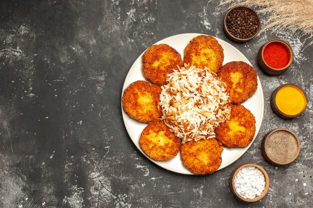 Vista dall'alto cotolette fritte con riso cotto e condimenti sulla carne della foto del piatto del cibo del pavimento scuro