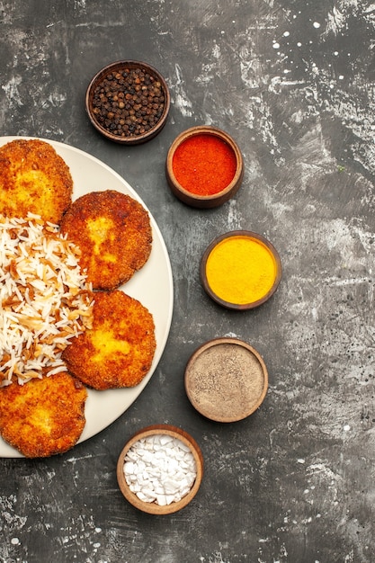 Vista dall'alto cotolette fritte con riso cotto e condimenti sulla foto del piatto di cibo con superficie scura