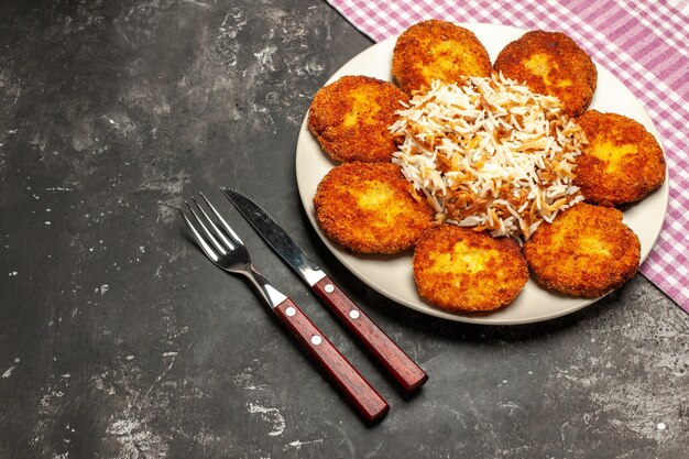 Vista dall'alto cotolette fritte con riso cotto su polpetta di piatto di carne scura scrivania