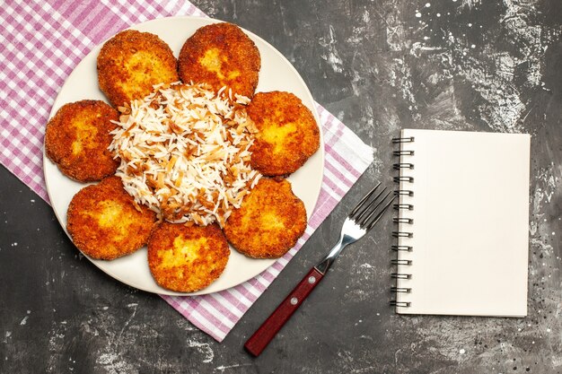 Vista dall'alto cotolette fritte con riso cotto sul piatto di polpetta di carne superficie scura