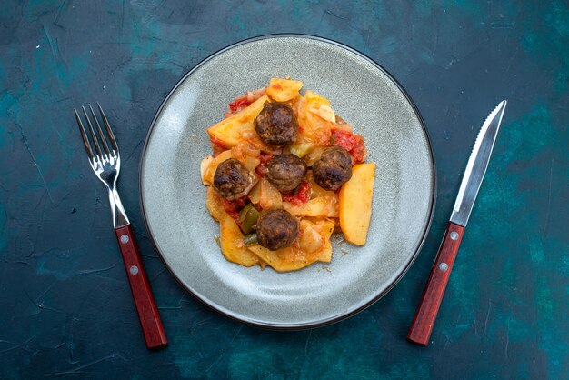 Vista dall'alto cotte patate a fette con polpette di carne all'interno del piatto sulla scrivania blu scuro.