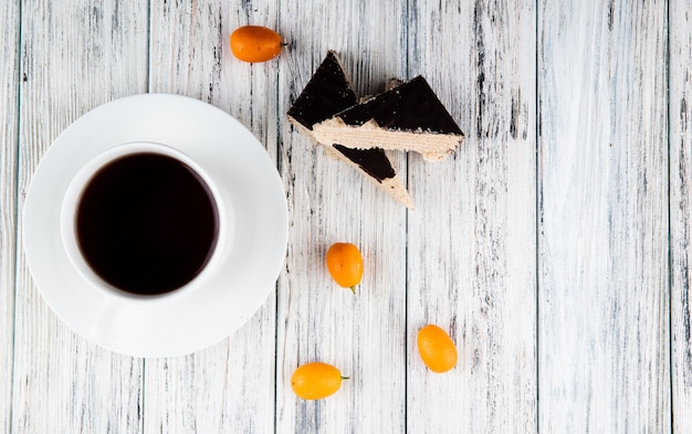 vista dall'alto Crunchy waffle cake sulla sinistra con tazza di caffè kumquat e copia spazio su fondo di legno bianco