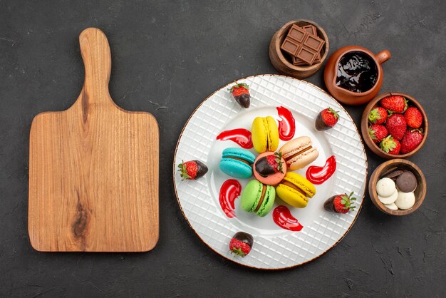 Vista dall'alto da lontano dessert amaretti e fragole nel piatto accanto al tagliere e ciotole con fragole al cioccolato e crema al cioccolato sul tavolo