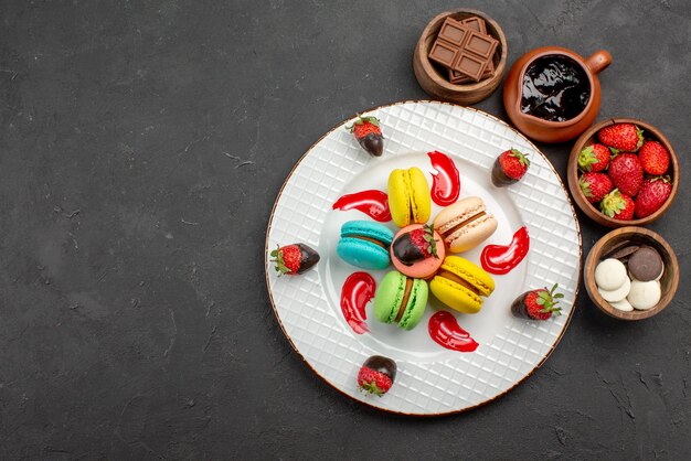 Vista dall'alto da lontano dessert gustosi amaretti e fragole accanto alle ciotole con fragole al cioccolato e crema al cioccolato sul lato destro del tavolo