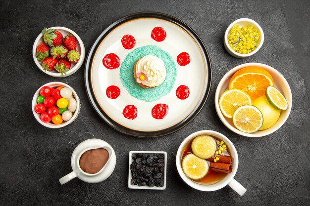 Vista dall'alto da lontano dolci con piatto da tè di appetitoso cupcake accanto alla tazza di tisane ciotole di crema al cioccolato fragole agrumi e caramelle