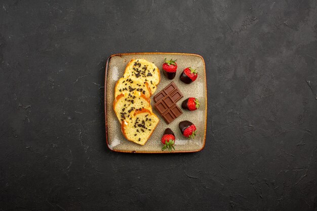 Vista dall'alto da lontano pezzi di torta appetitose fragole ricoperte di cioccolato e pezzi di torta al cioccolato su un piatto quadrato sul tavolo scuro