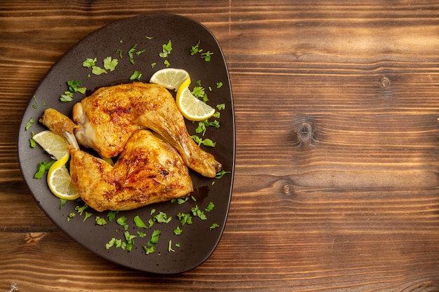 Vista dall'alto da lontano pollo con cosce di pollo al limone con erbe e limone nel piatto sul lato sinistro del tavolo