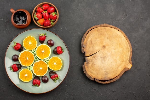 Vista dall'alto da lontano salsa di cioccolato e arancia e fragole accanto a caramelle verdi arancioni tritate alla fragola ricoperte di cioccolato e tagliere di legno