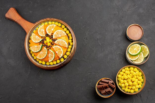 Vista dall'alto da lontano torta di lime e caramelle con agrumi sul lato sinistro e ciotole di diversi dolci fette di lime sul lato sinistro del tavolo nero